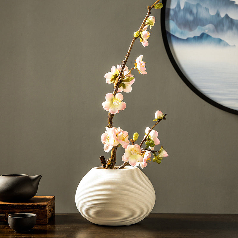 Soft pink artificial plum blossom arrangement in a white ceramic vase, perfect for creating a warm and romantic atmosphere.