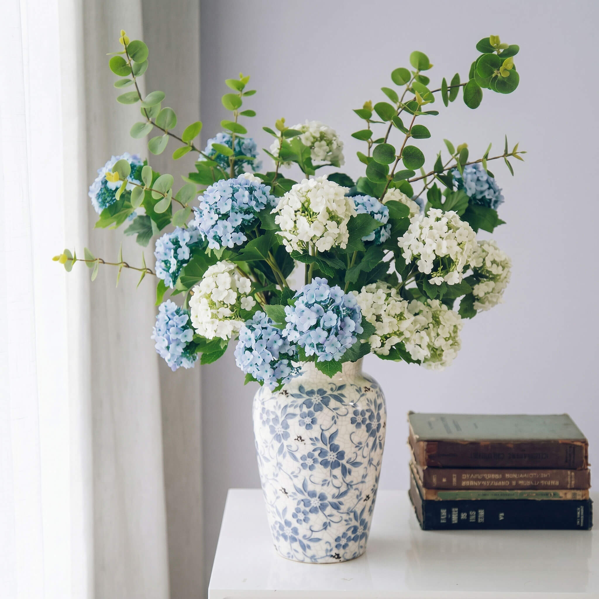 Artificial hydrangea arrangement in a blue and white porcelain vase, elegant faux floral centerpiece for home decor.
