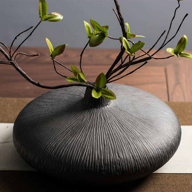 A faux multi-branch ficus stem placed in a black glazed ceramic vase, captured in a close-up shot of the ficus branch and the vase