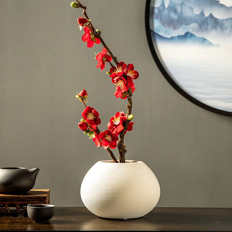 Artificial red plum blossom arrangement in a white ceramic vase, a vibrant floral centerpiece for elegant home decor.