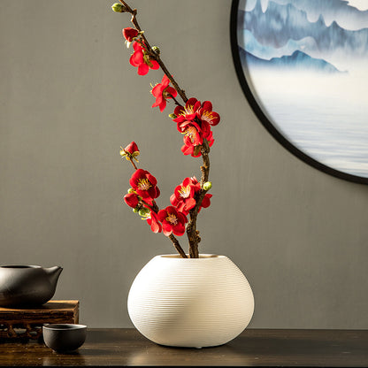Artificial red plum blossom arrangement in a white ceramic vase, a vibrant floral centerpiece for elegant home decor.