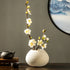 White artificial plum blossom arrangement in a ceramic vase, offering a clean and minimalist decorative accent.