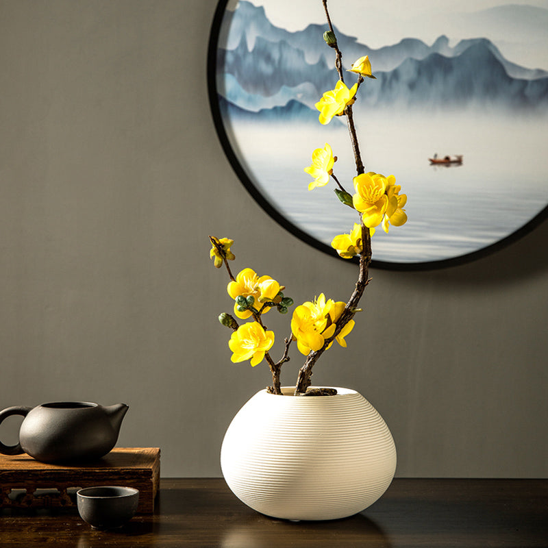Yellow artificial plum blossom arrangement styled in a white ceramic vase, adding a bright and cheerful touch to interiors.