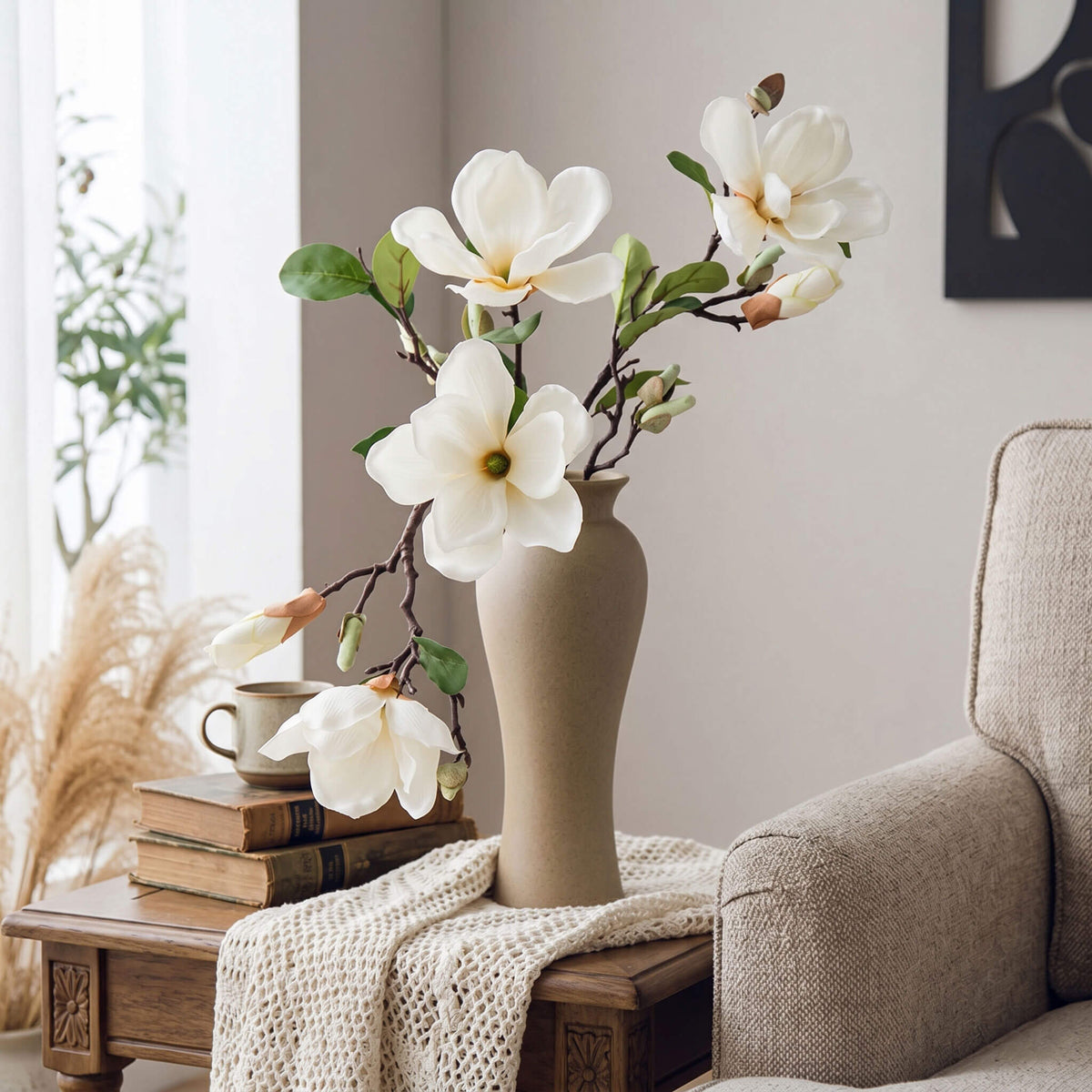 Faux magnolia arrangement styled in a living room, displayed on a side table with a curved pale yellow vase.