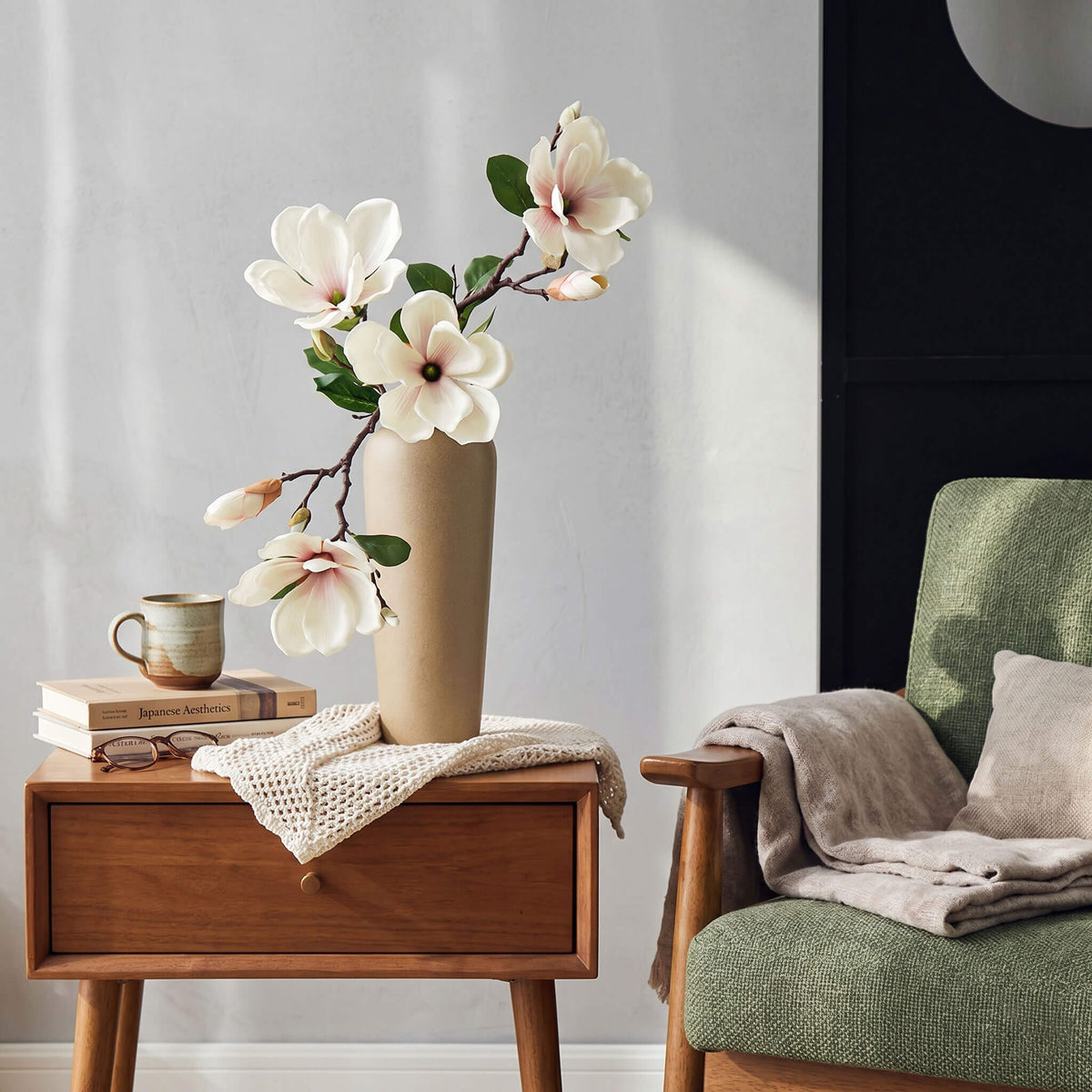 Artificial magnolia arrangement styled in a living room, placed on a sofa table with a pale yellow vase for a soft elegant look.